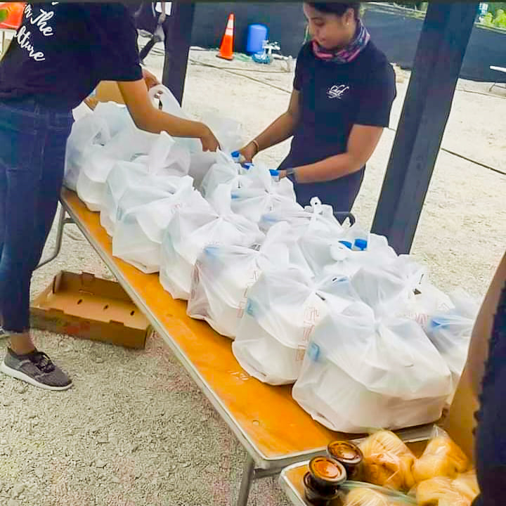 Two people organizing white bags on a table outdoors.